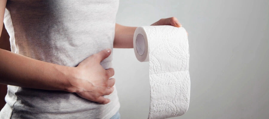Mulher com papel higiênico nas mãos correndo para o banheiro com diarreia e fezes moles.