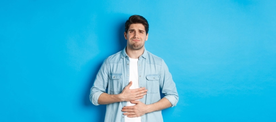 um homem com uma camisa azul e jeans de pé contra uma parede azul