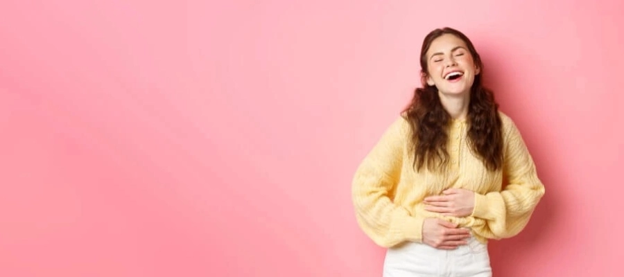 Fundo rosa e uma mulher sorridente vestindo blusa amarela com as mãos na barriga