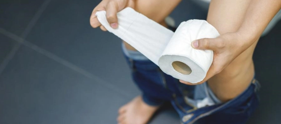 uma pessoa segurando um rolo de papel higiênico sentada no vaso