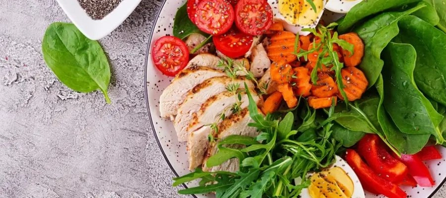 Prato representando uma dieta saudável com tomate cereja, peito de frango, ovos, cenoura, salada com rúcula e espinafre.webp