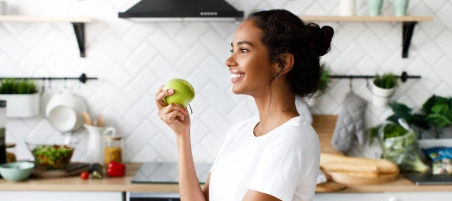 mulher jovem na cozinha de casa comendo mação verde para ganho de peso