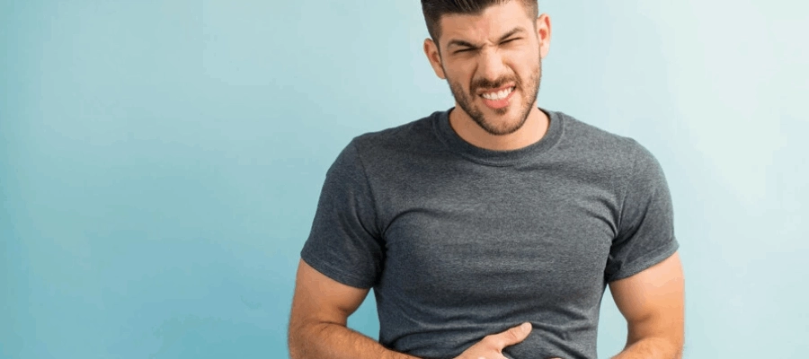 homem com blusa cinza tem as mãos na barriga e expressão de dor com sintoma de diarreia aguda