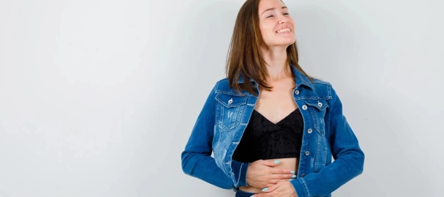 mulher jovem com jaqueta jeans com as mãos na barriga sorrindo feliz