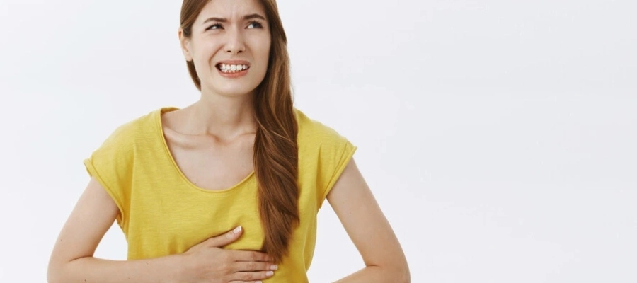 mulher jovem com blusa amarela com as duas mãos na barriga sentindo desconforto abdominal