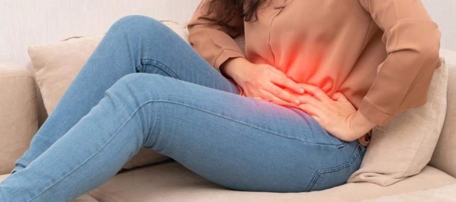 mulher de jeans sentada no sofá com cólica