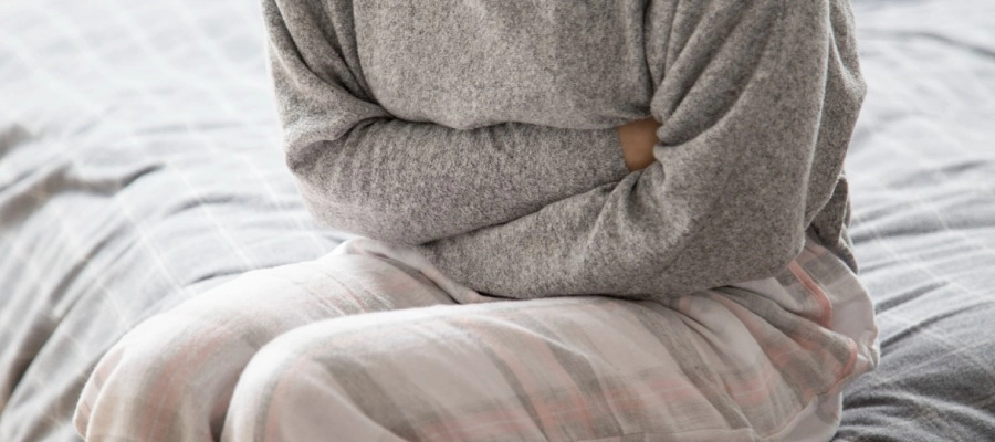 pessoa de moletom sentada na cama com dor na barriga