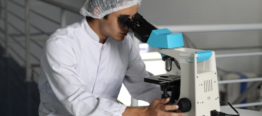 homem em laboratório olha pelo microscópio