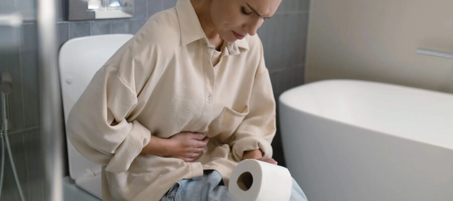 Mulher sentada no vaso sanitário com dor de estômago e pontinhos brancos nas fezes.